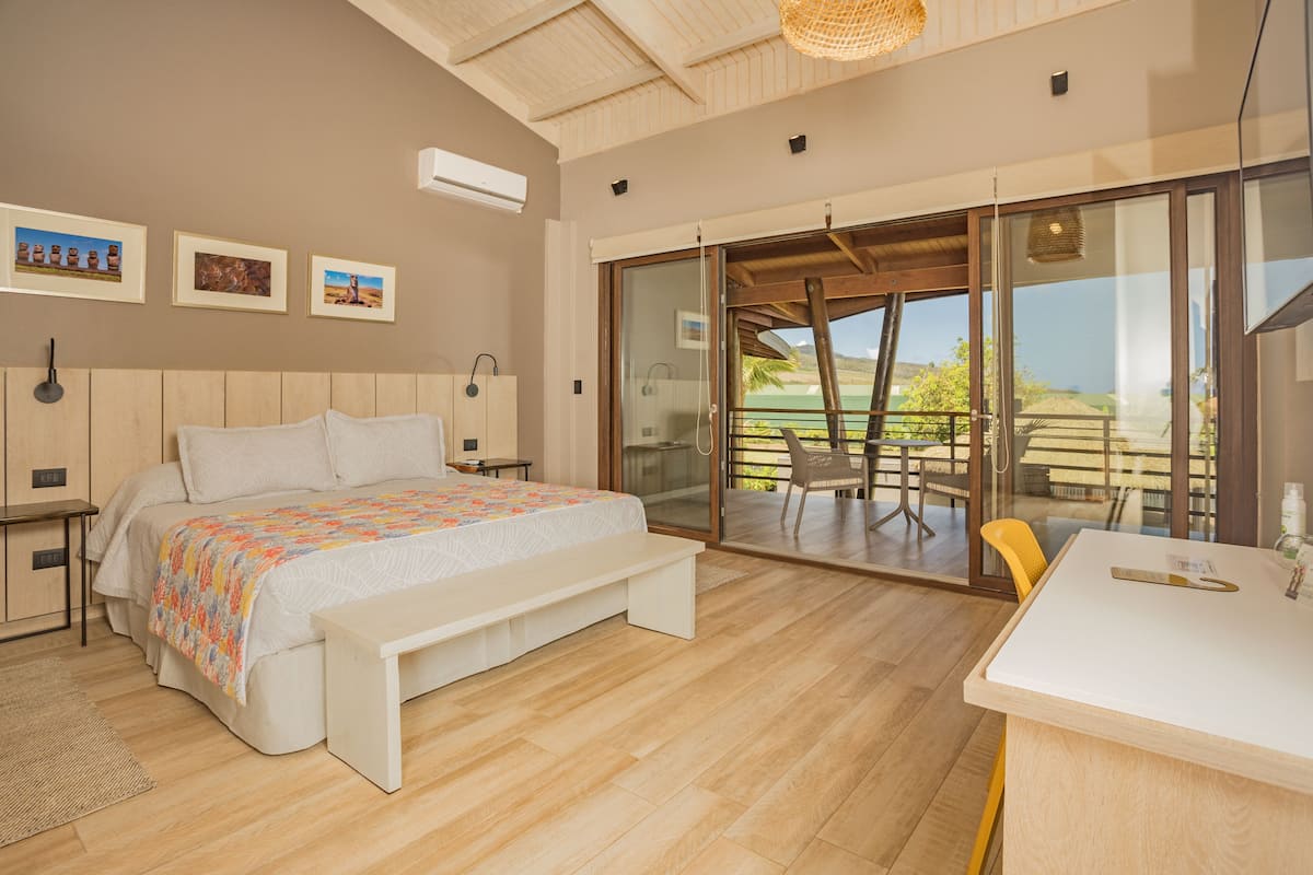 A bedroom with a large bed, a desk, and a sliding glass door leading to a balcony.