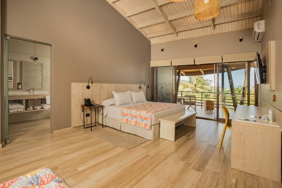 A modern bedroom with a bed, bedside table, and a large window offering a view of the outdoors.