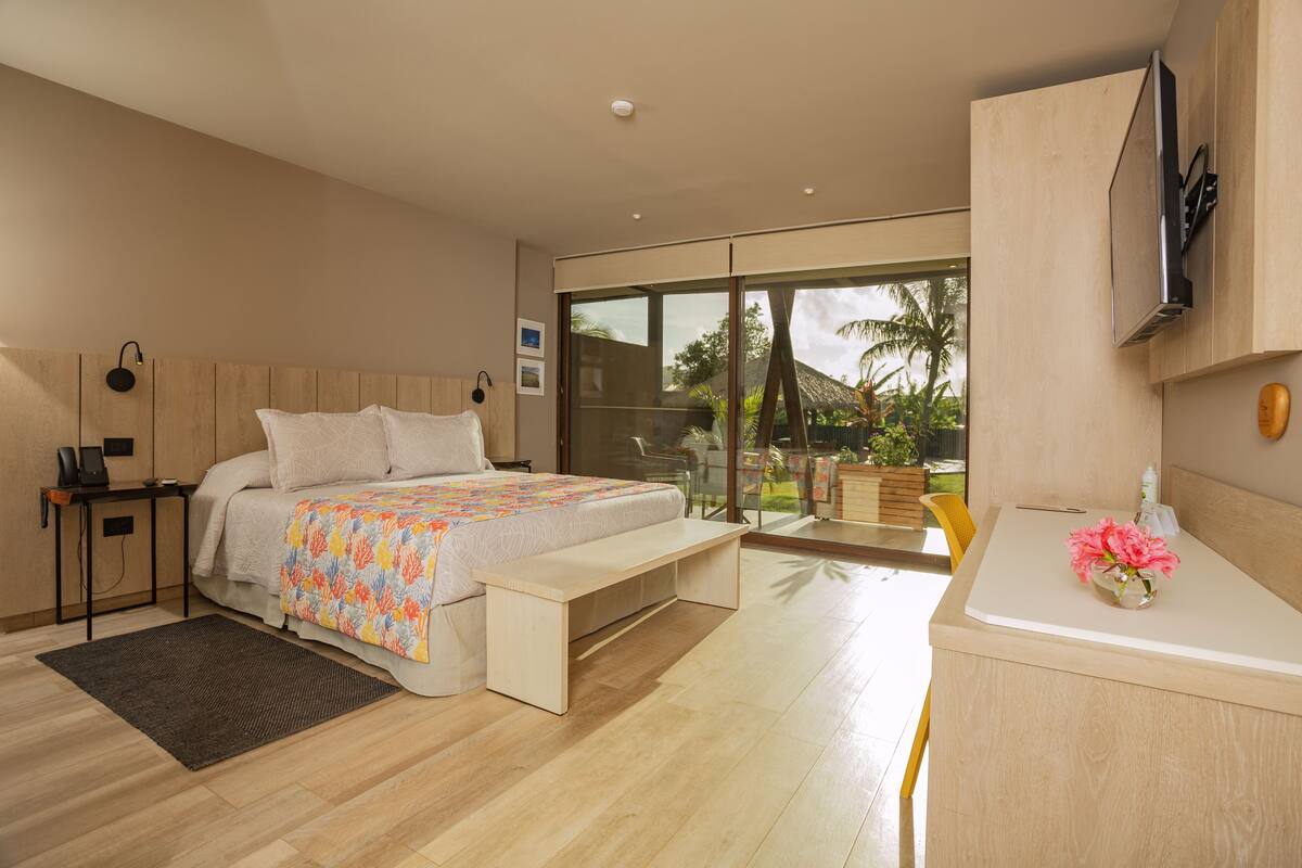 A modern bedroom with a bed, bedside table, bench, and a view of the outdoors.