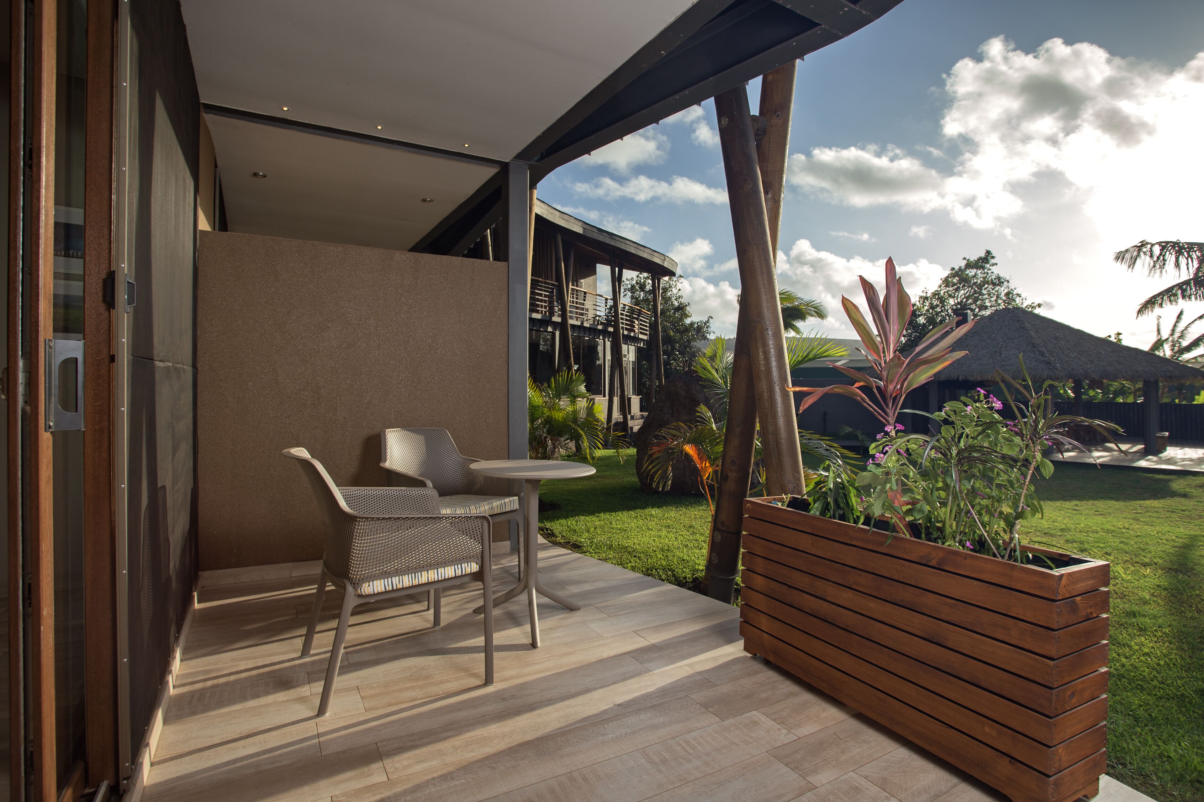 Een modern terras buiten met een zithoek, een houten plantenbak en uitzicht op een huis en tuin.