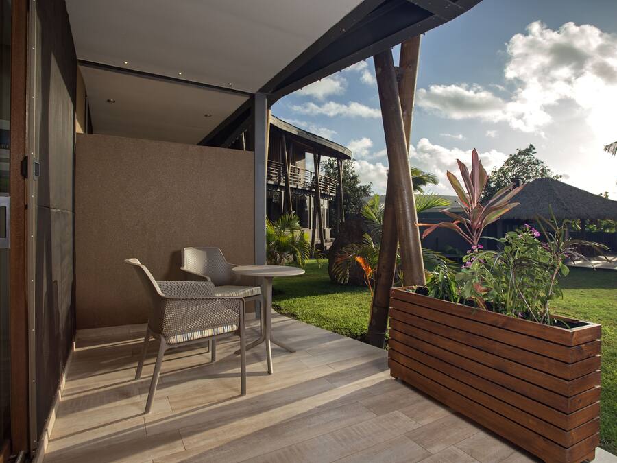Een modern terras buiten met een zithoek, een houten plantenbak en uitzicht op een huis en tuin.