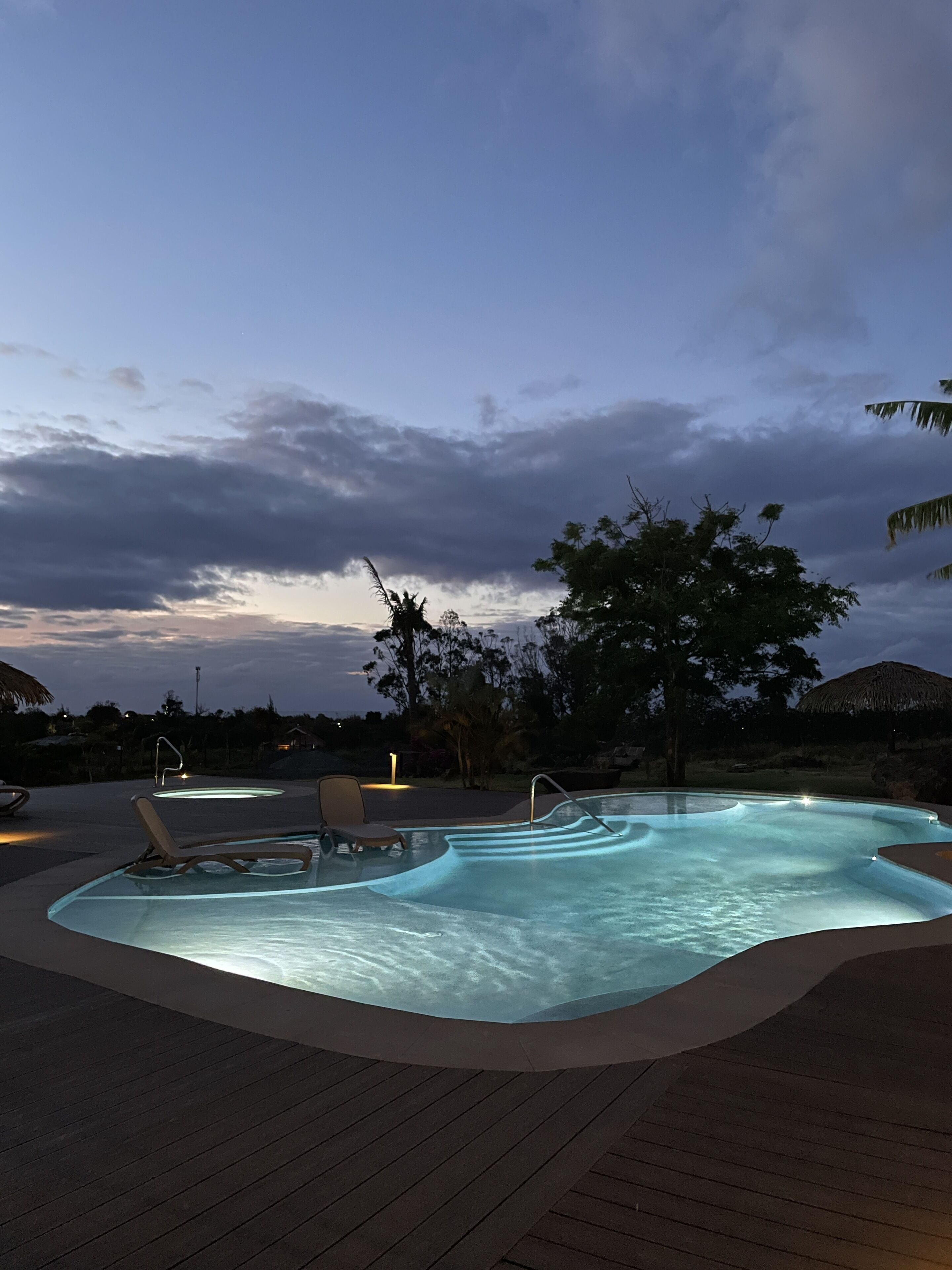 A swimming pool with a curved edge, surrounded by lounge chairs and a wooden deck.