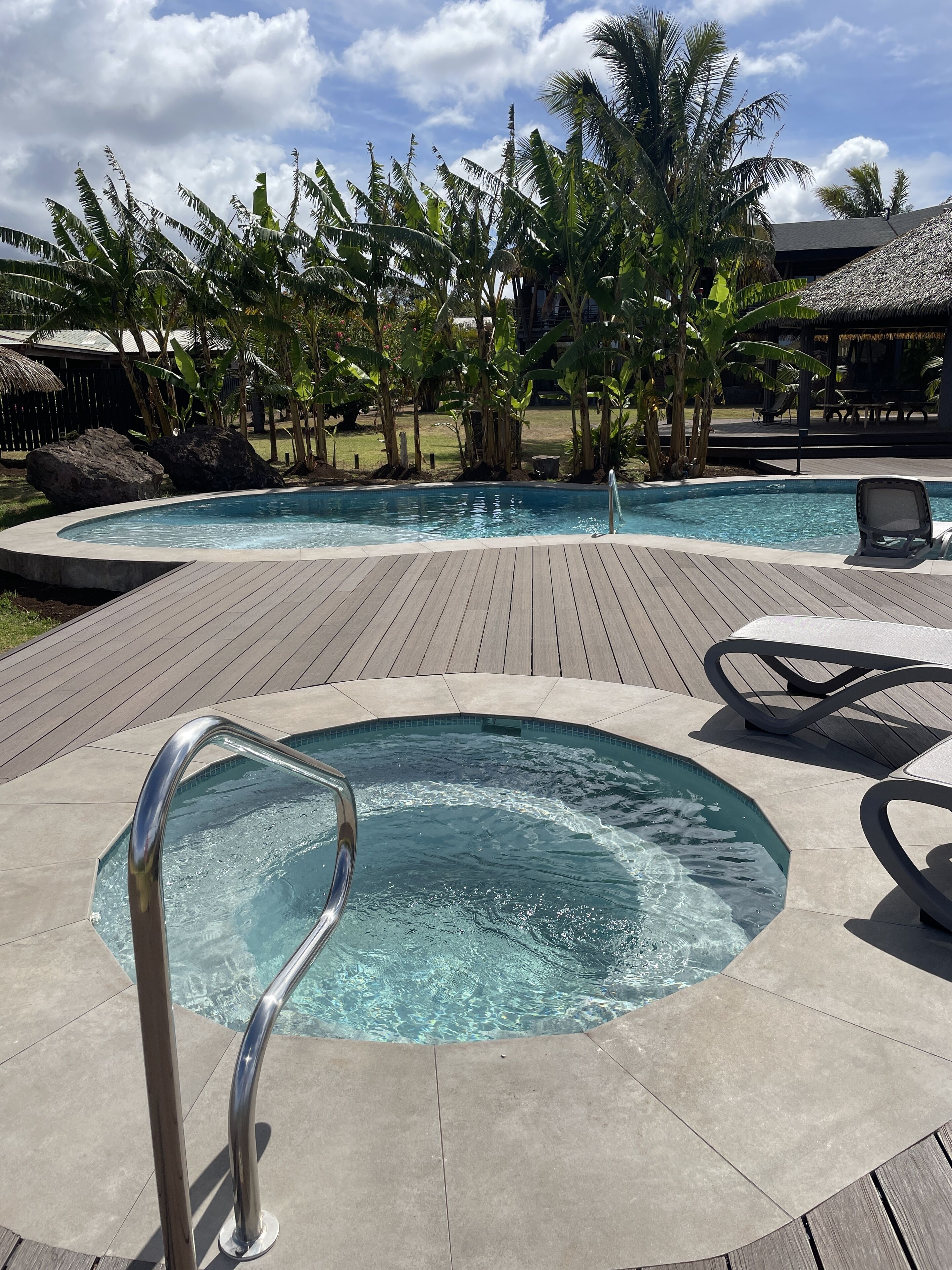 A swimming pool with a wooden deck, lounge chairs, and tropical vegetation.