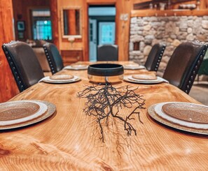 A wooden dining table with a centerpiece of black branches, surrounded by chairs with black leather seats and metal accents. - Stunning custom bld-riverside-pet/family friendly (Intervale)