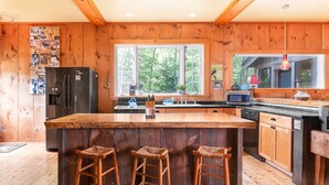 Una cocina con armarios de madera, una isla grande con taburetes, un refrigerador y una ventana con vistas a árboles.