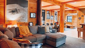 Interior acogedor de una cabaña de madera con un amplio sofá modular, un comedor y un letrero visible que dice 'SPY'.