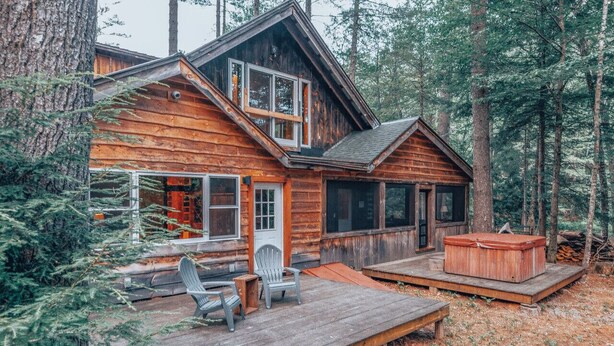 Una cabaña rústica con un balcón, dos sillas Adirondack y un jacuzzi.