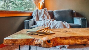Una habitación acogedora con una mesa de centro de madera, un sofá gris y una ventana con vistas a árboles.