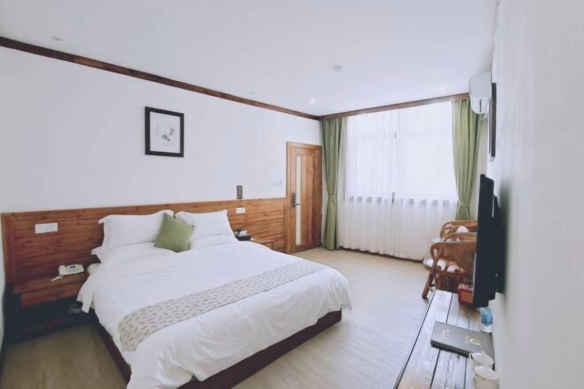 Une chambre d’hôtel avec un grand lit, une tête de lit en bois, une télévision et une fenêtre avec des rideaux.