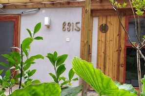 Puerta de madera con el número 8315, pared blanca y follaje verde al frente.