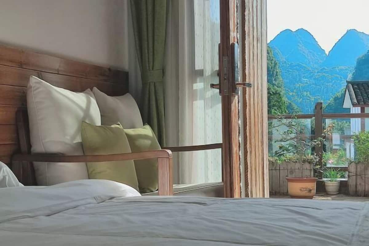 Une chambre à coucher avec une tête de lit en bois, du linge de lit blanc et une vue sur les montagnes, visible à travers une porte-fenêtre coulissante.