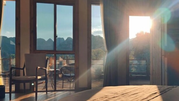 A room with large windows, a wooden floor, and a view of mountains. - Tianla Bayin Inn (Xingyi)