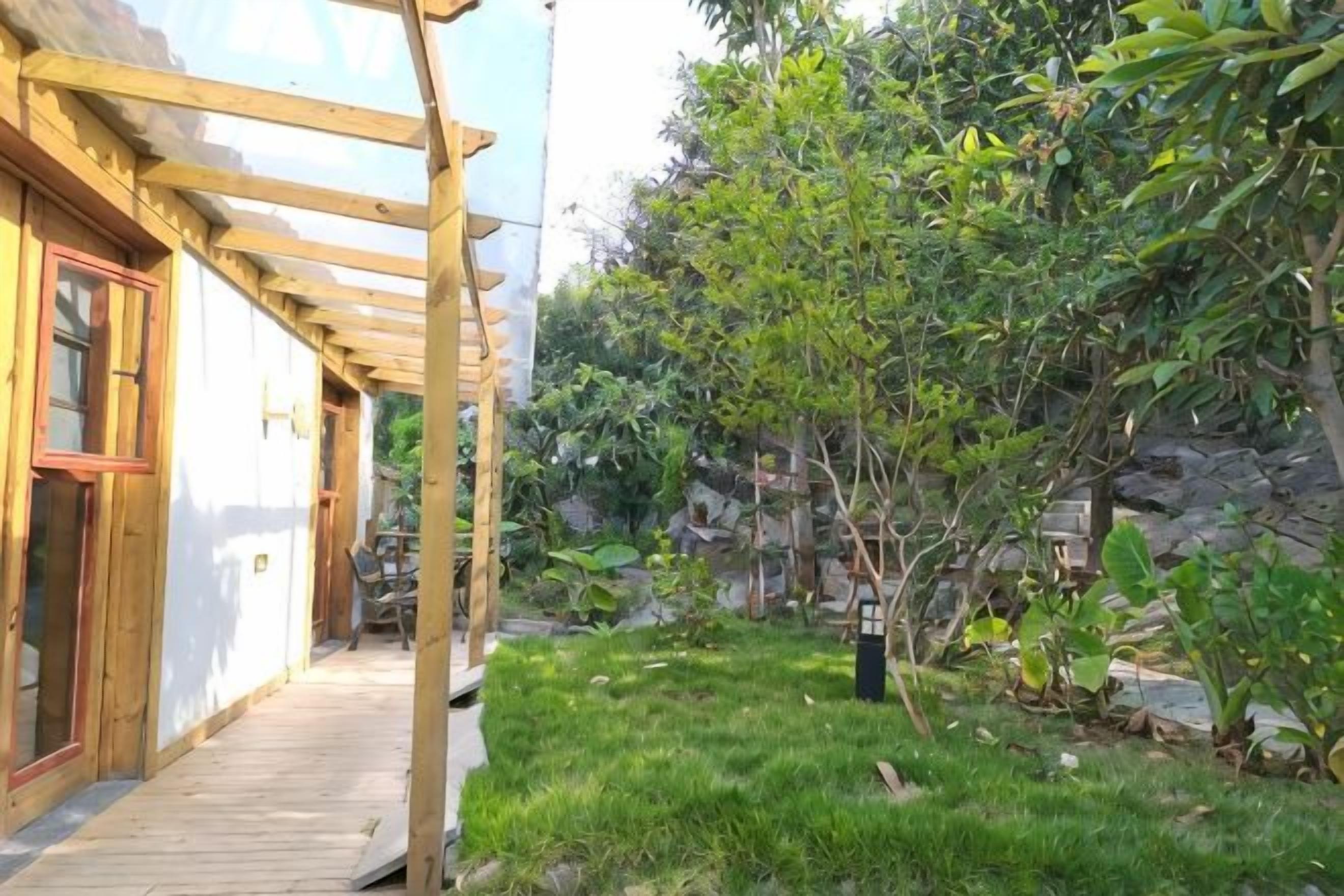 En pergola av trä över en uteplats med en gräsyta och en stenmur i bakgrunden.