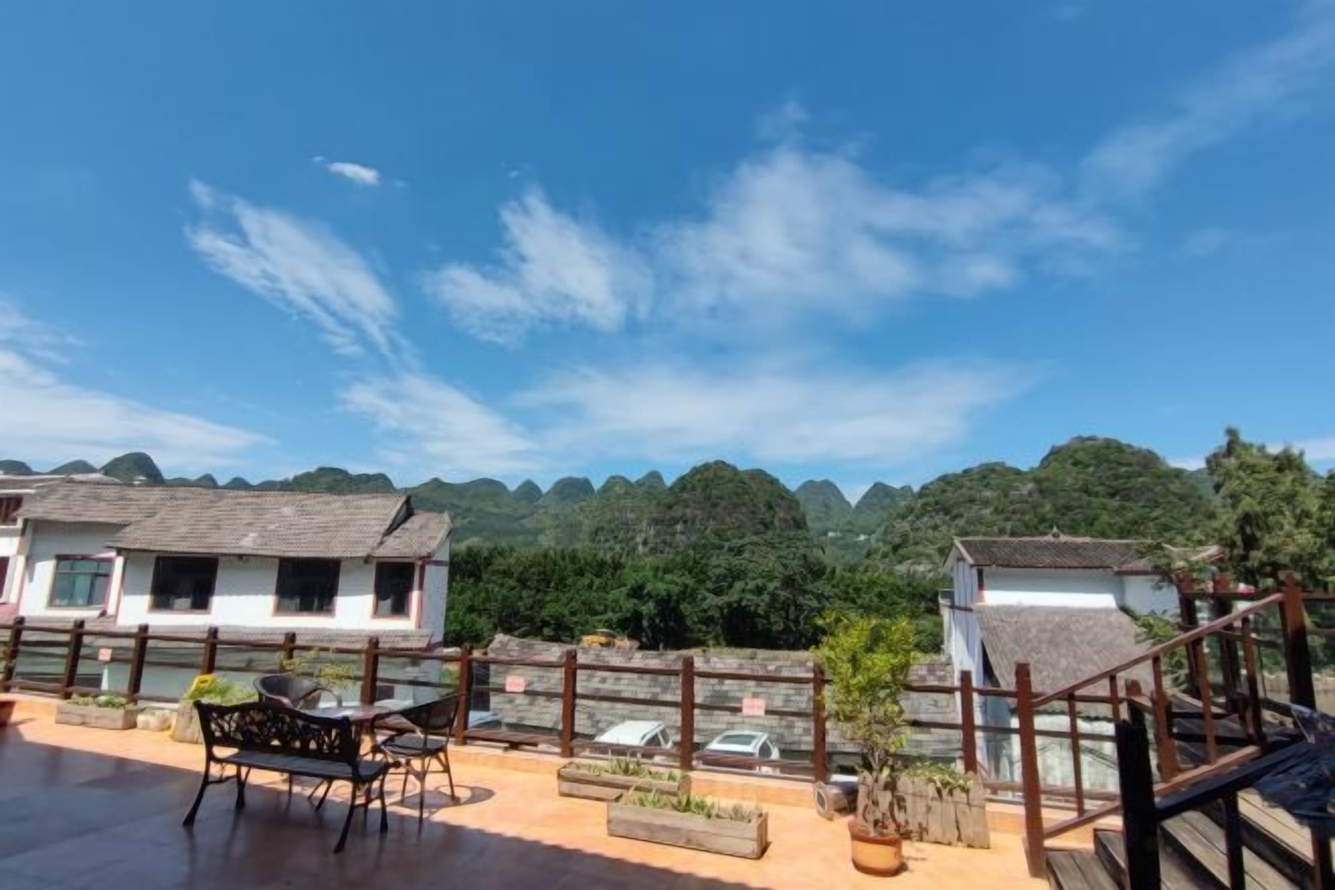 A terrace with a table and chairs, overlooking a mountainous landscape with buildings in the background.
