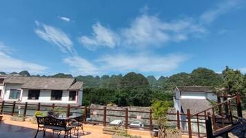 A terrace with a table and chairs, overlooking a mountainous landscape with buildings in the background.