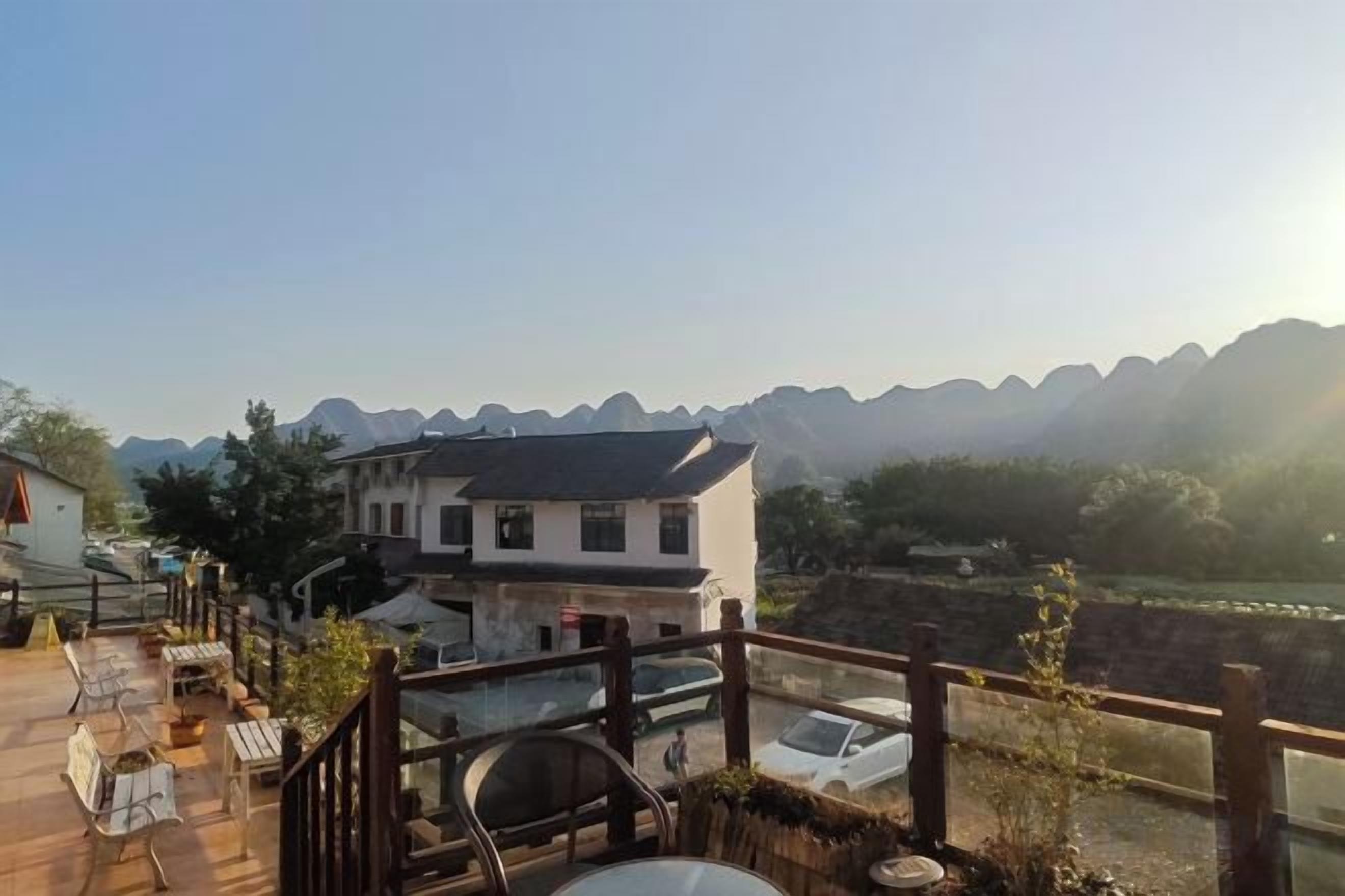 A wooden deck with outdoor seating, a building with a traditional design, and a view of distant mountains.