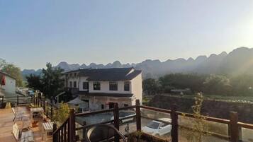 A wooden deck with outdoor seating, a building with a traditional design, and a view of distant mountains.