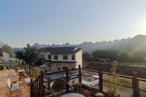 Una terraza de madera con mobiliario exterior, un edificio de diseño tradicional y vistas a montañas distantes.