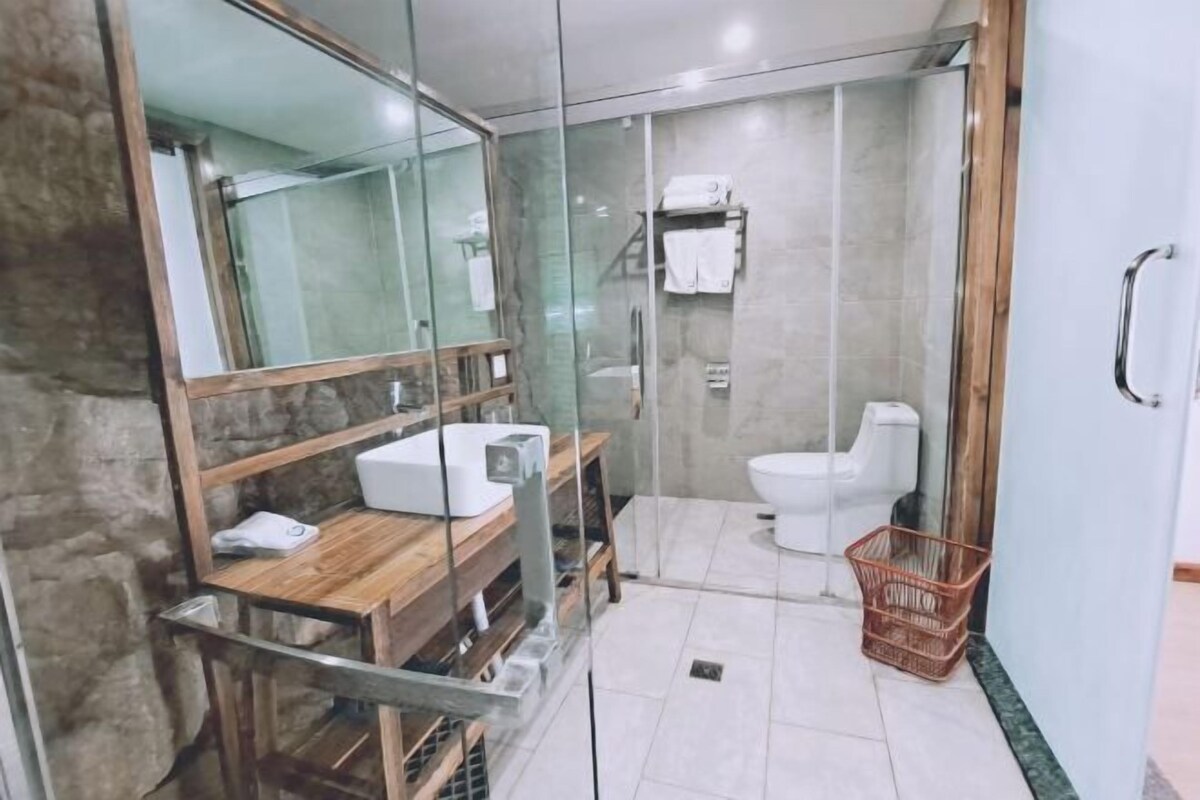 Een moderne badkamer met een glazen douchecabine, een houten wastafelmeubel, een wit toilet en een klein rieten mandje.