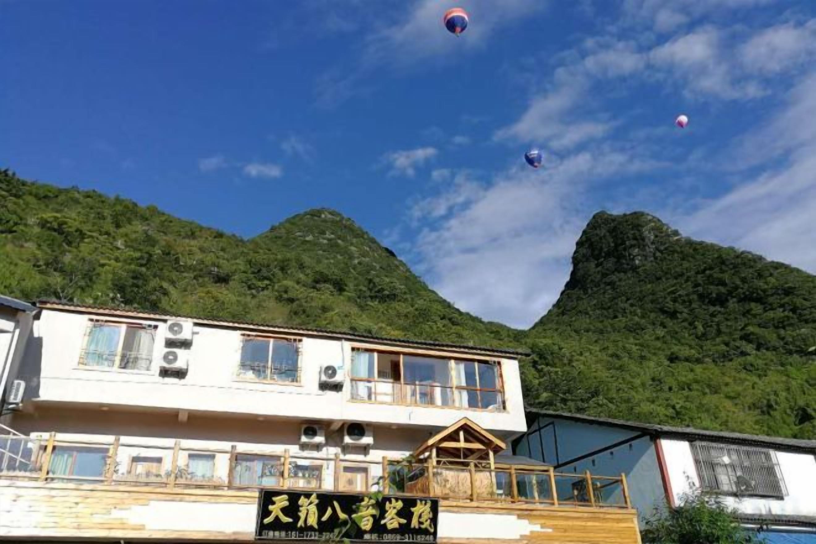 A building with multiple windows and a signboard, surrounded by lush green hills.