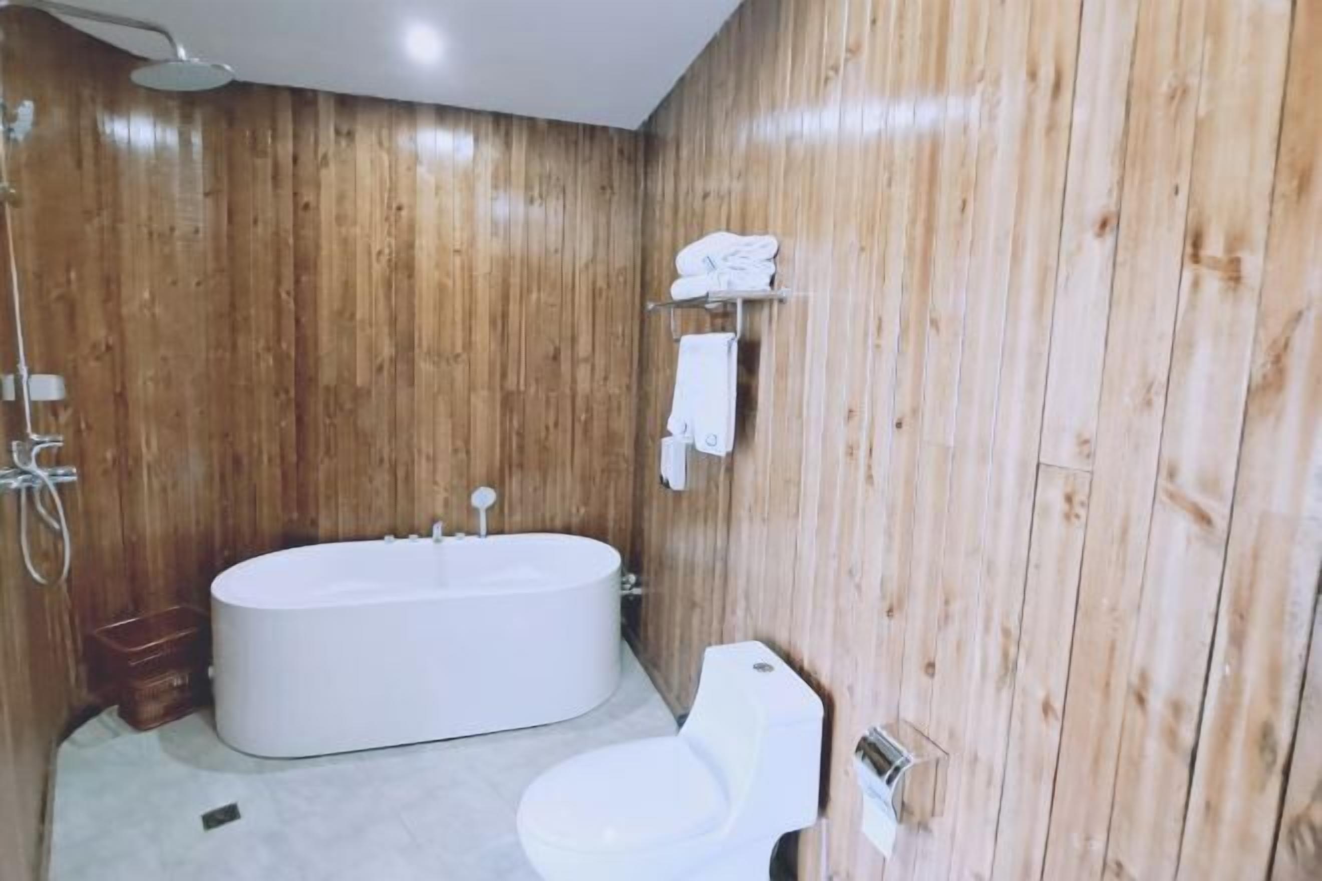 Un baño con paneles de madera, una bañera, un inodoro y un perchero con toallas.