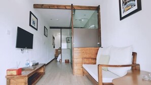 A modern hotel room with a wooden sofa, a small wooden table, a TV mounted on the wall, and a glass door leading to a balcony. - Tianla Bayin Inn (Xingyi)