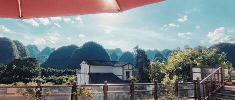 Eine Terrasse mit Kübelpflanzen, einem roten Sonnenschirm und Blick auf eine gebirgige Landschaft.