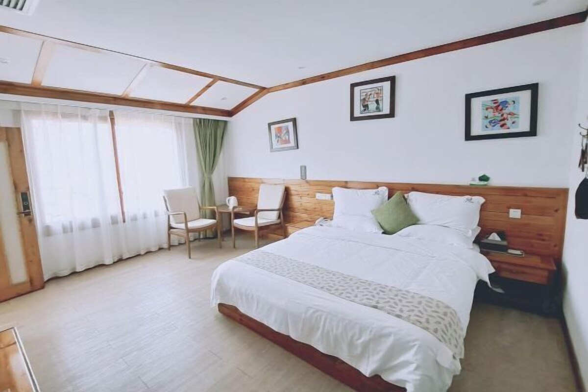 Een slaapkamer met een bed, twee stoelen, een houten hoofdbord en kunst aan de muur.