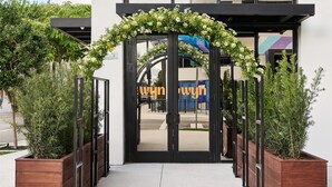 A modern building entrance with a wooden planter walkway, a clear sky, and a reflection of a building in the glass facade. - Arlo Wynwood Miami (Miami)