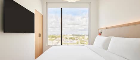 Una camera d'albergo moderna con un letto grande, una TV a schermo piatto montata a parete e vista sulla città dalla finestra.