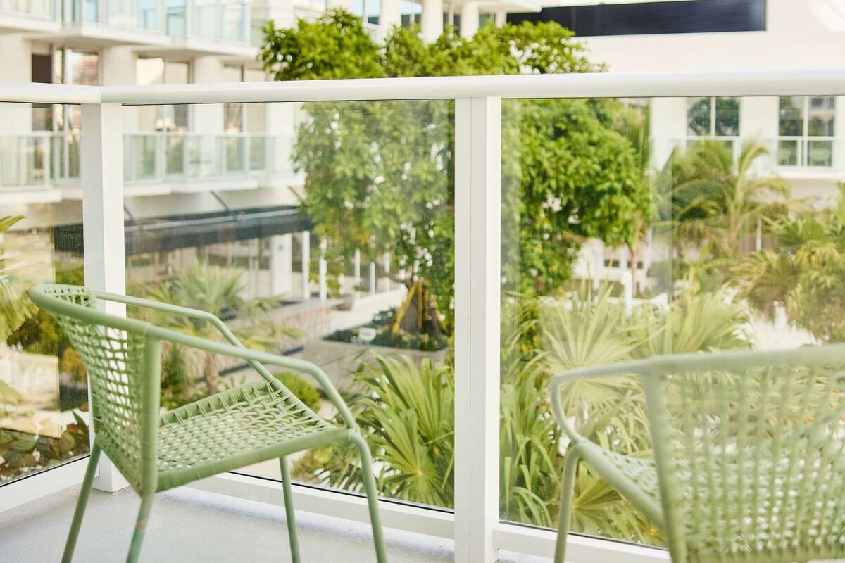 A balcony with two green chairs and a view of a modern building with balconies.