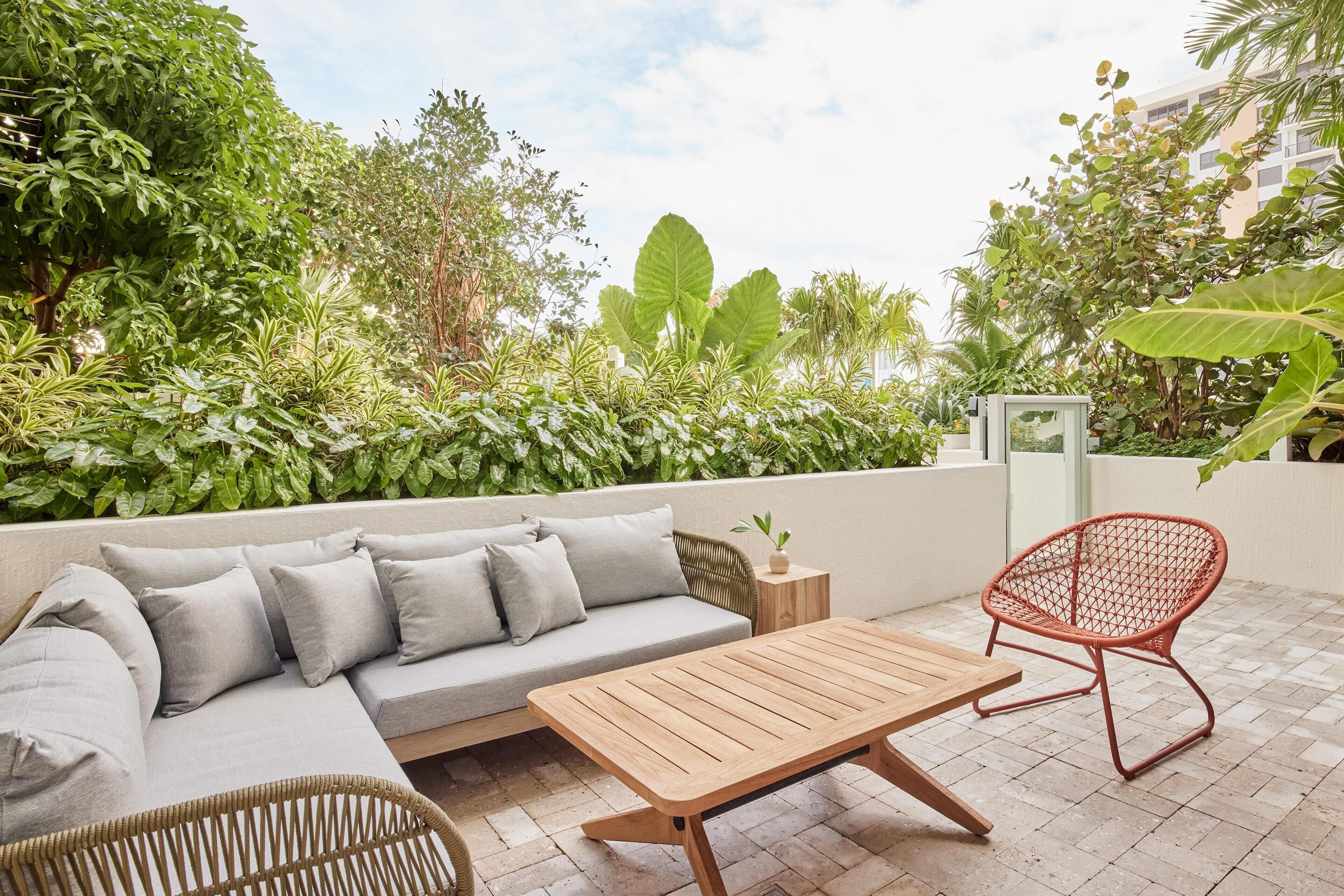 Un patio con un sofá, una mesa de madera y una silla roja.
