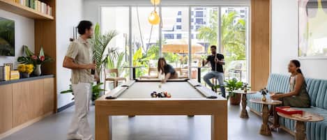 Una mesa de billar moderna en un espacio interior, con un área de estar informal que incluye un sofá y una mesita con aperitivos.