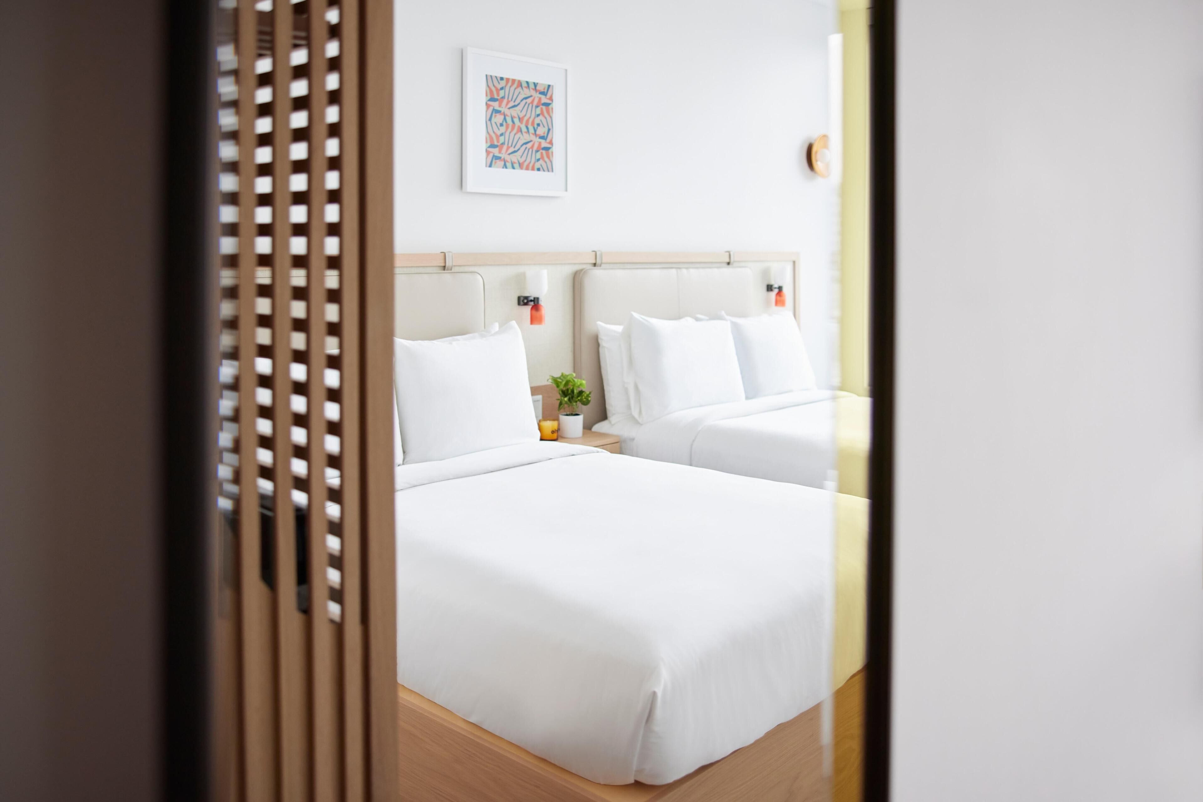 Ein Hotelzimmer mit zwei Betten, einem Nachttisch mit Pflanze und einem an der Wand hängenden Kunstwerk.