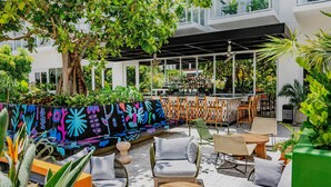An outdoor seating area with wicker furniture, a bar, and lush greenery. - Arlo Wynwood Miami (Miami)