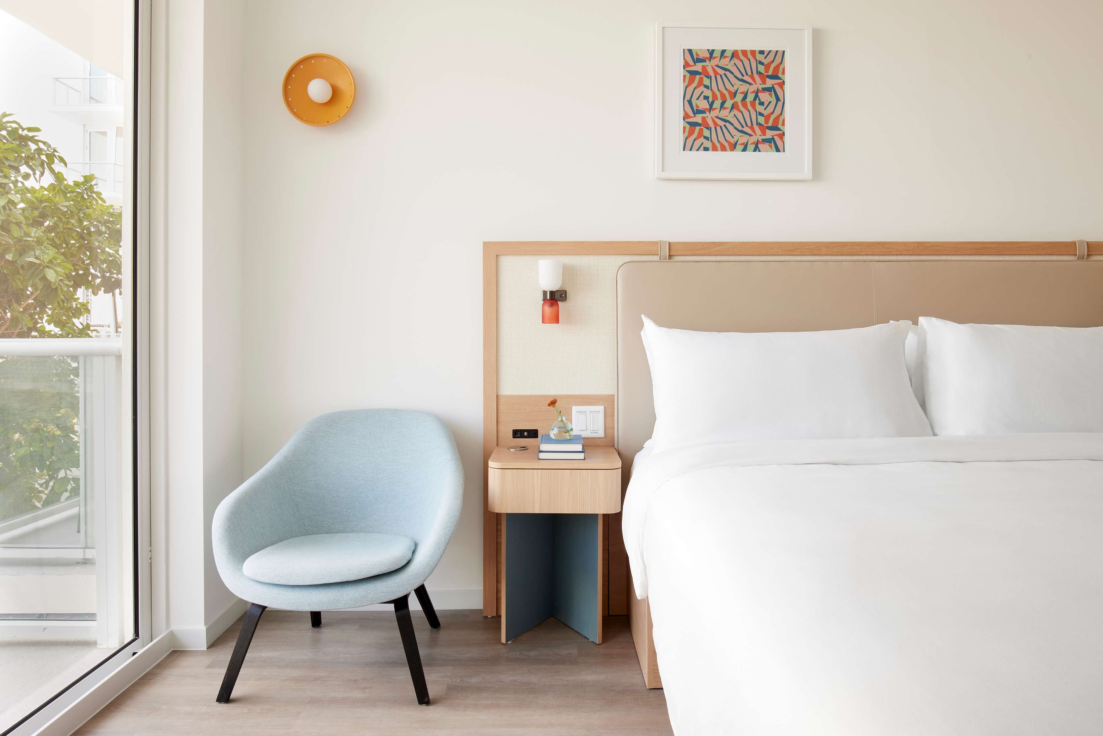 Ett hotellrum med en säng, ett skrivbord, en stol, ett fönster och ett konstverk som hänger på väggen.