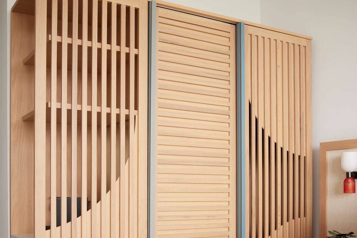 A modern bedroom with a wooden wardrobe featuring vertical slats and a central panel.