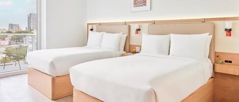 A hotel room with two beds, a city view, a framed artwork, and a nightstand with a lamp.