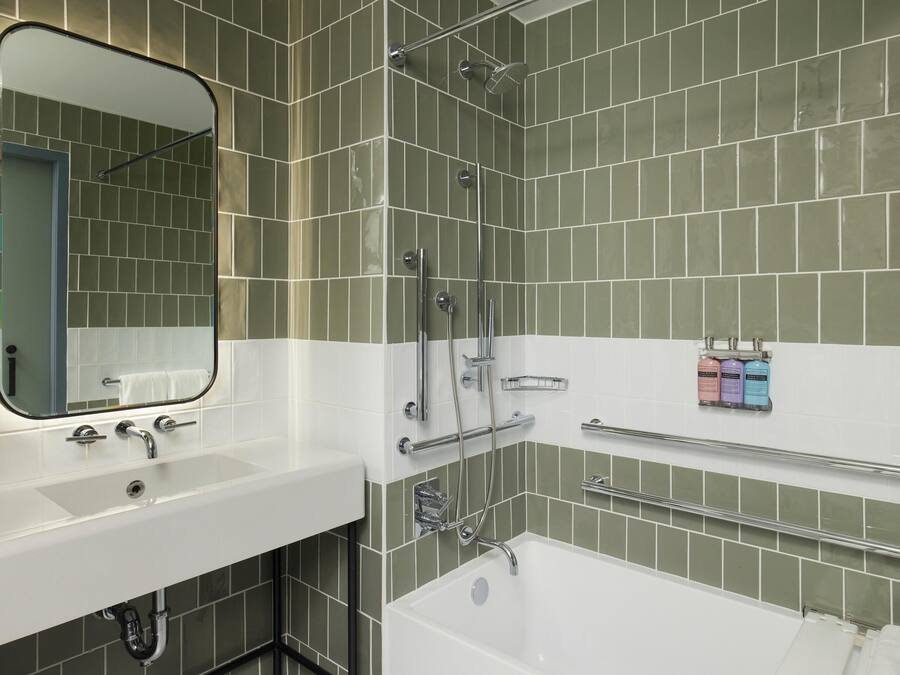 A bathroom with a white sink, a mirror, a shower with chrome fixtures, and a towel rack with toiletries.