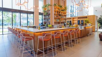 A modern bar area with a long counter, multiple bar stools, and shelves stocked with bottles.