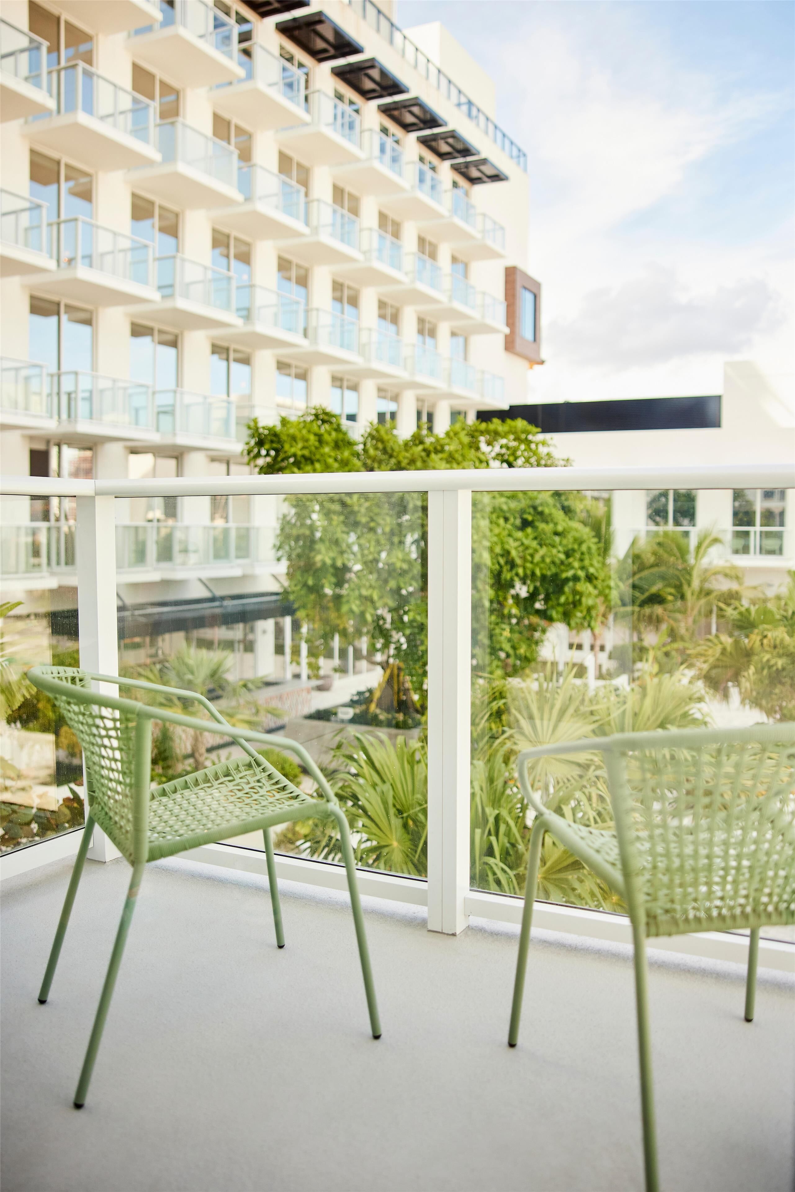 A balcony with two green chairs, a glass railing, and a view of a building with multiple balconies.