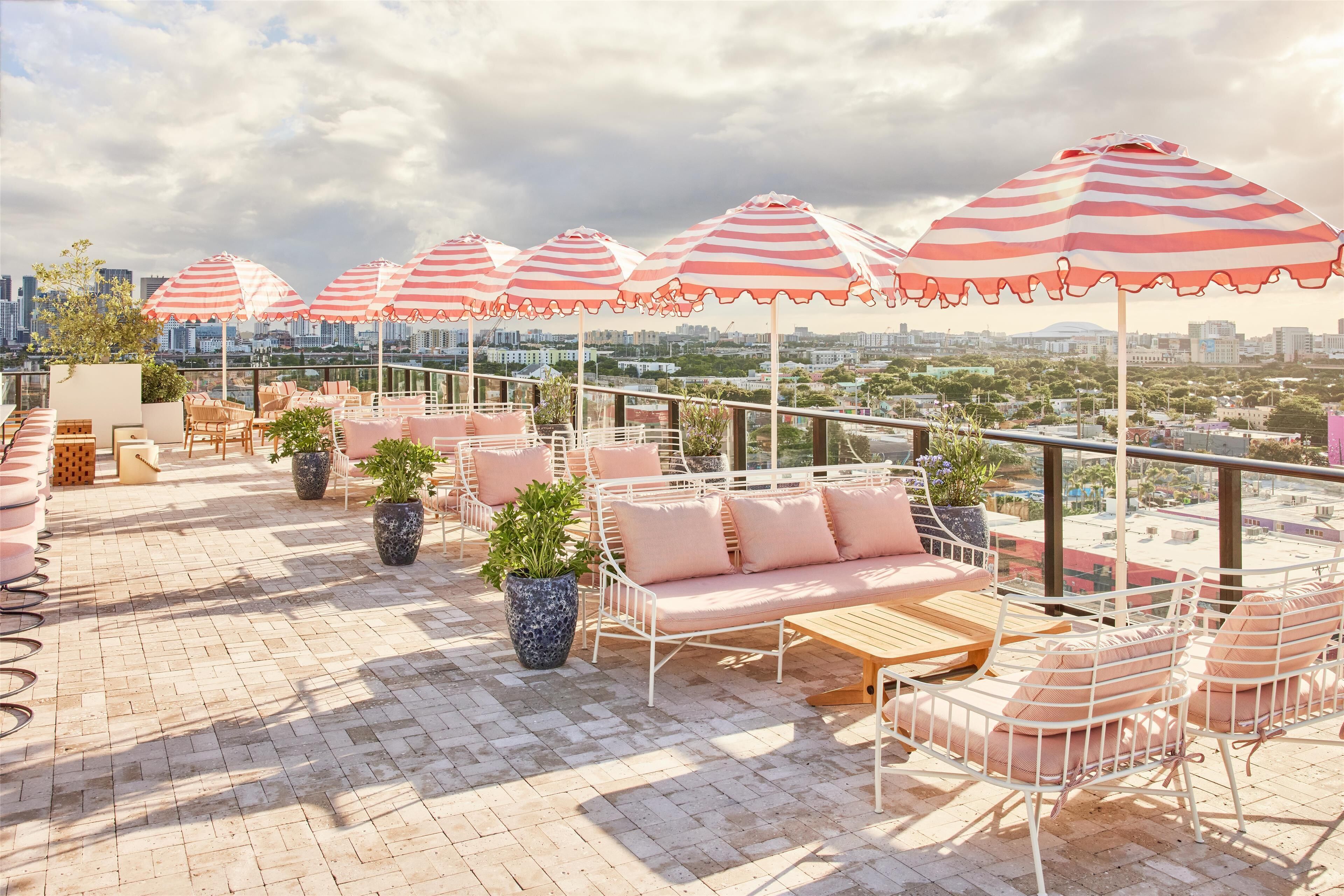 A rooftop terrace with striped umbrellas, seating areas, and potted plants.