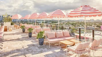 A rooftop terrace with striped umbrellas, seating areas, and potted plants.