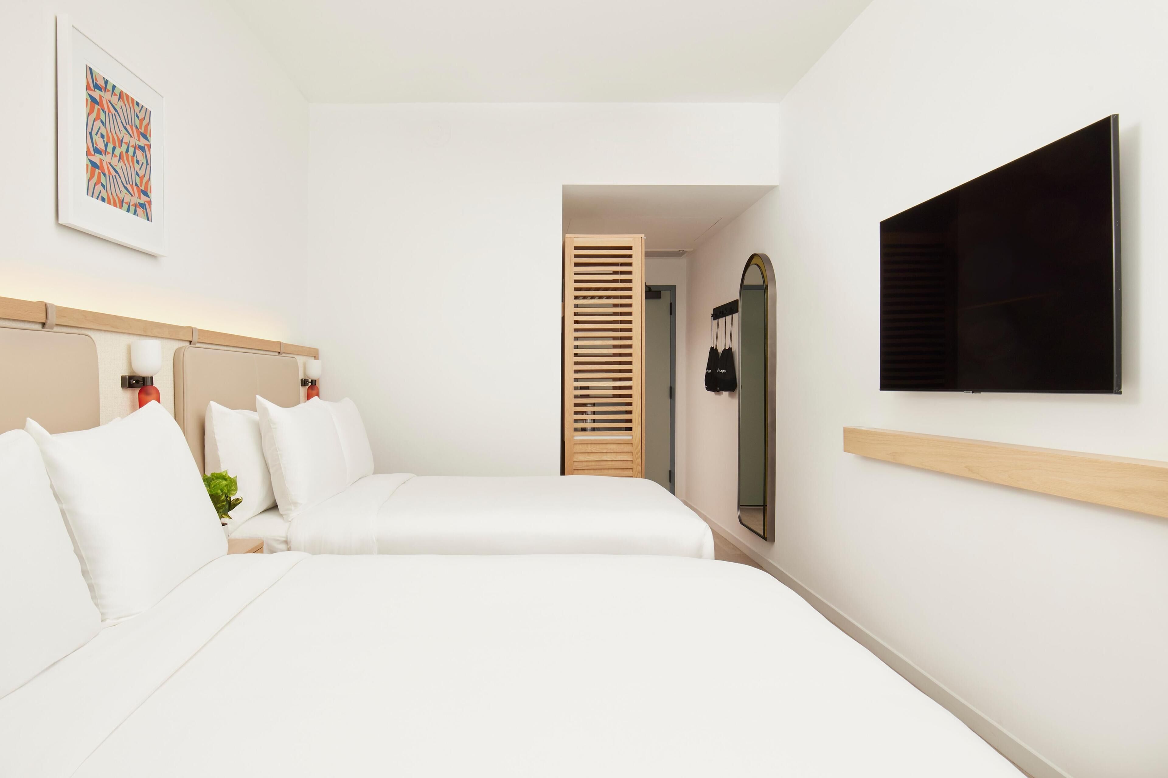 A hotel room with a bed, a TV, a mirror, and a door leading to another room.