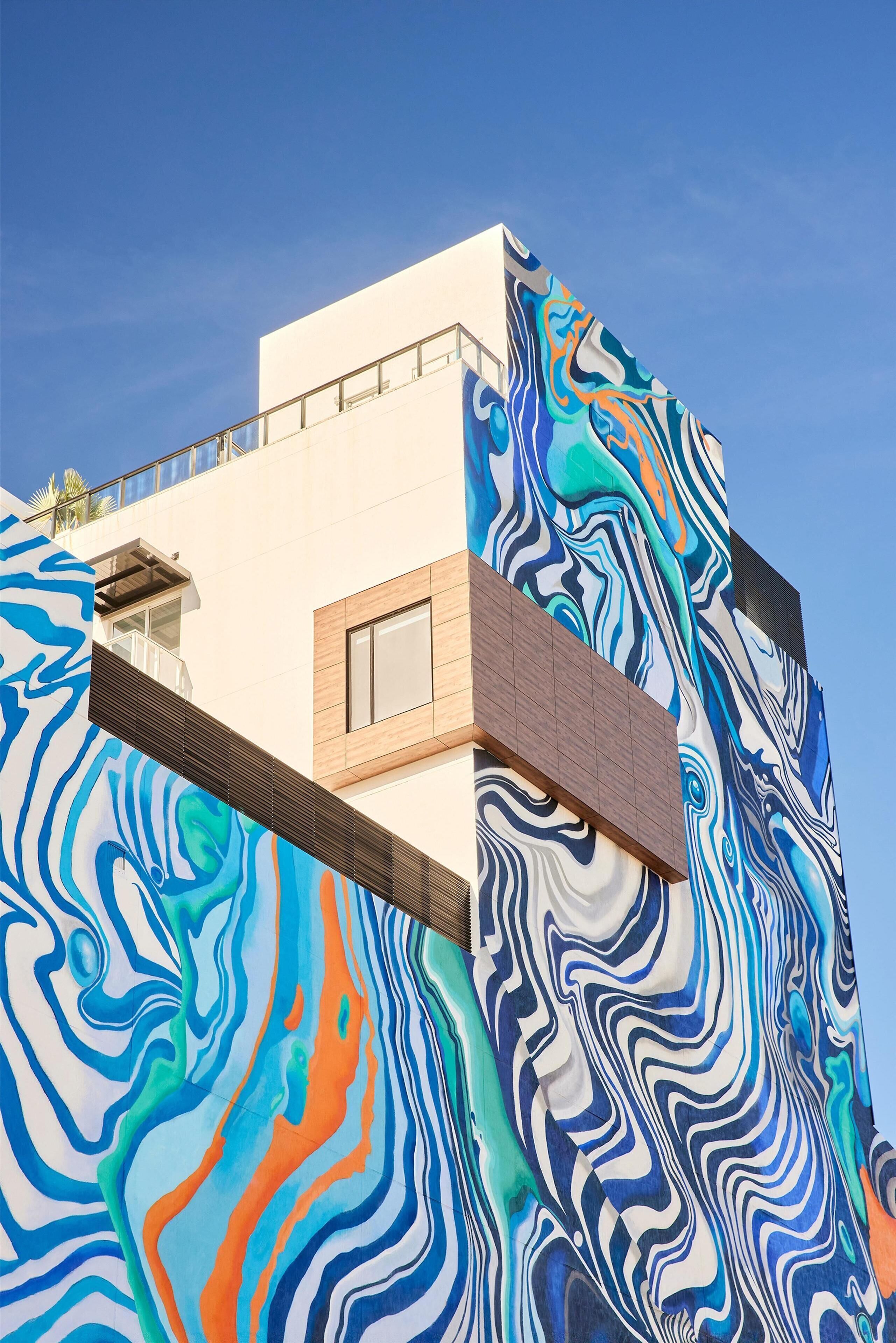 Un edificio con un diseño arquitectónico moderno y un mural grande y colorido en su fachada.