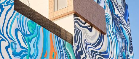 Un edificio con un diseño arquitectónico moderno y un mural grande y colorido en su fachada.