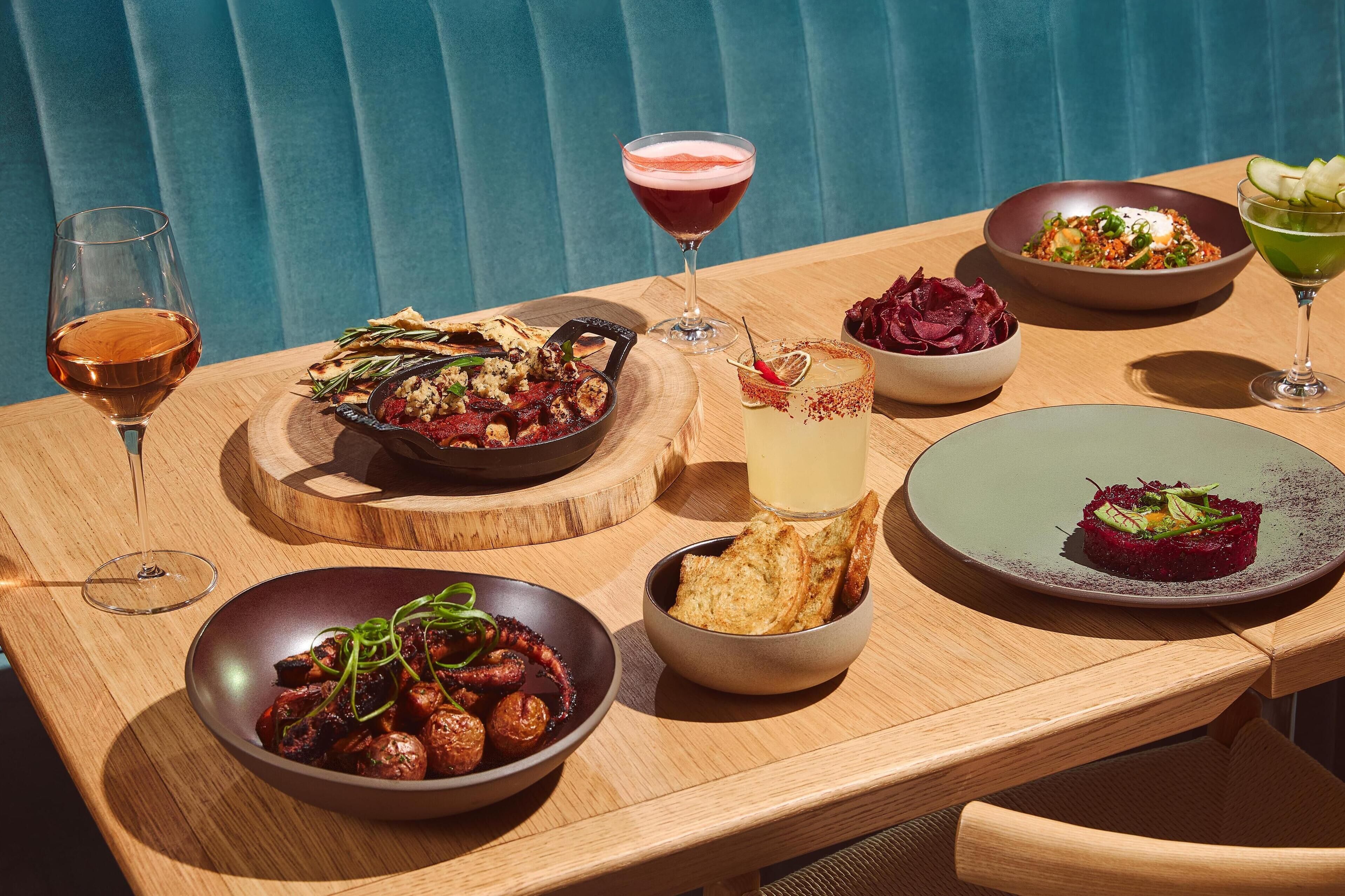 Una mesa de madera con varios platos y bebidas, incluyendo pulpo, una ensalada y un plato de remolacha.