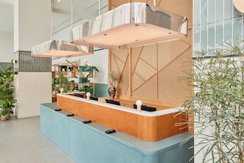 A hotel room with a bed, a bedside table with a plant, a mounted TV, and a large mirror reflecting the room. at Arlo Wynwood Miami