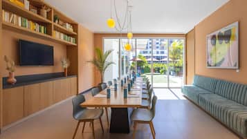 A modern dining area with a long table, chairs, a bookshelf, a flat-screen TV, and a sofa.