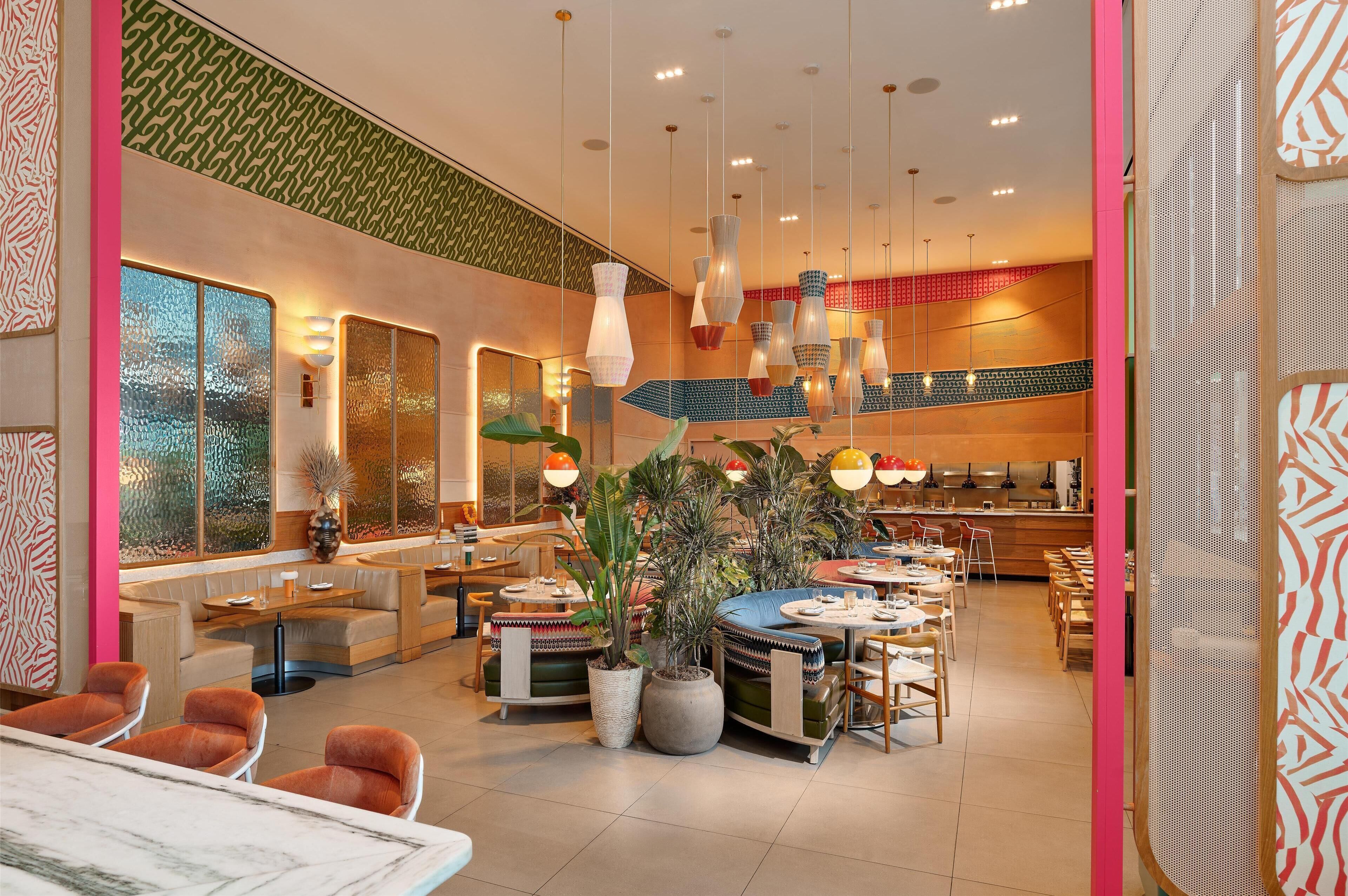 Un restaurante moderno con varias zonas de estar, incluyendo cabinas y mesas, y una cocina a la vista.